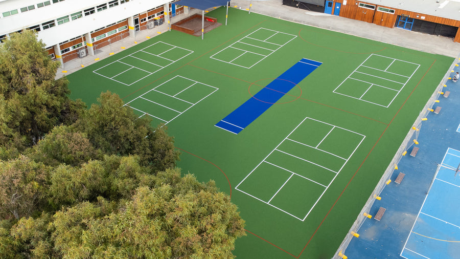 Aerial view of synthetic turf sports courts with white and blue markings at a school playground.