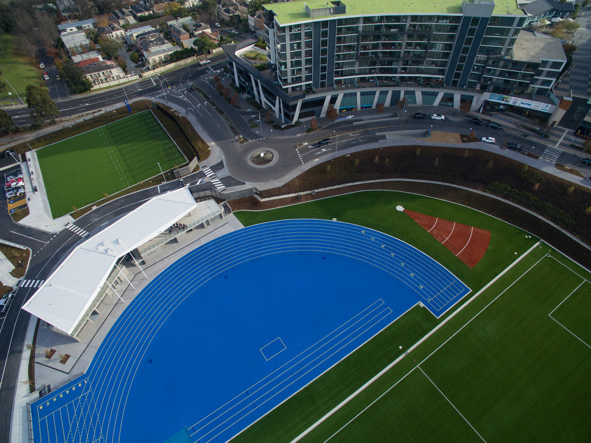 Aerial view of synthetic turf sports facility with blue running track and artificial grass fields.