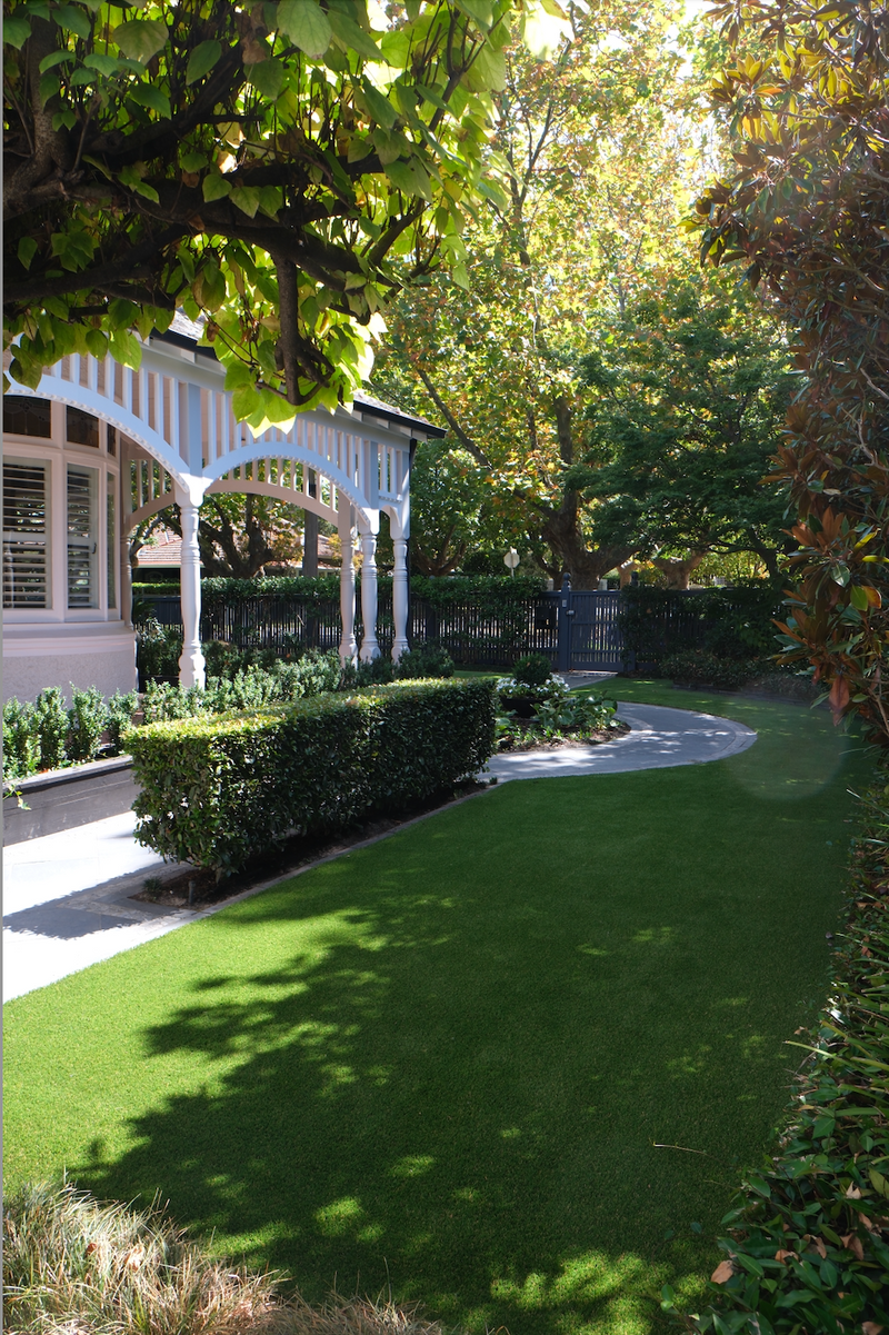 Lush artificial grass lawn in a residential garden with manicured hedges and a white veranda