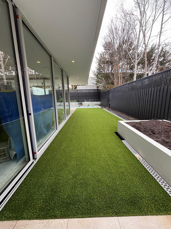 Residential backyard with artificial grass turf beside a modern patio and garden bed