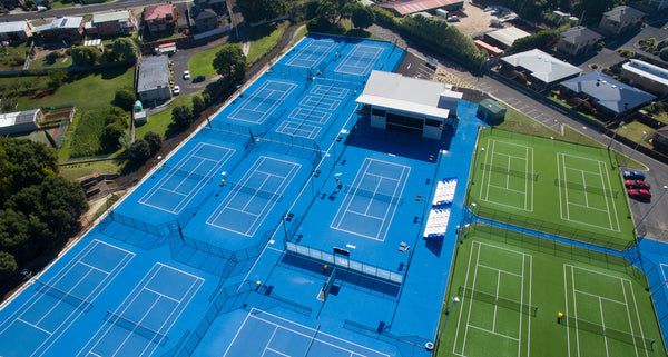 Aerial view of multiple blue hard tennis courts and green artificial turf courts at a sports facility