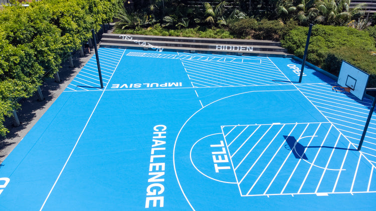 Blue outdoor basketball and netball court with motivational words, surrounded by greenery