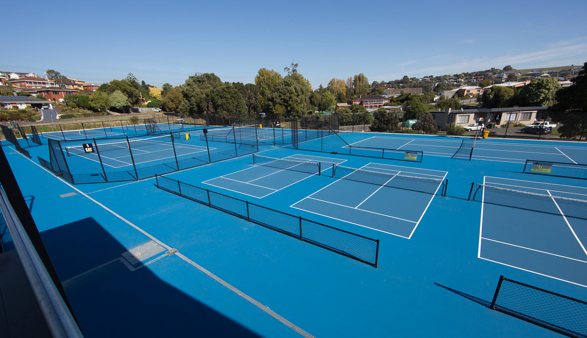 Multiple outdoor blue acrylic tennis courts with fencing in a residential area