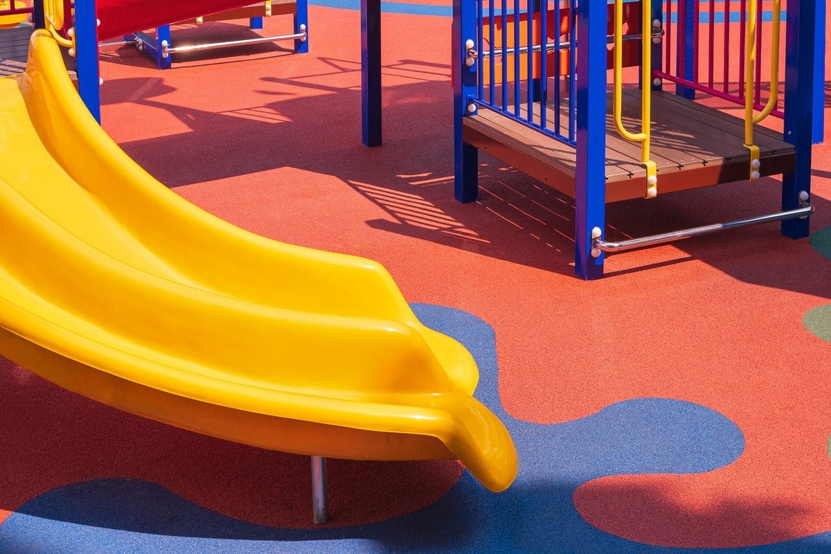 Yellow slide and colorful rubber softfall flooring at a childcare playground