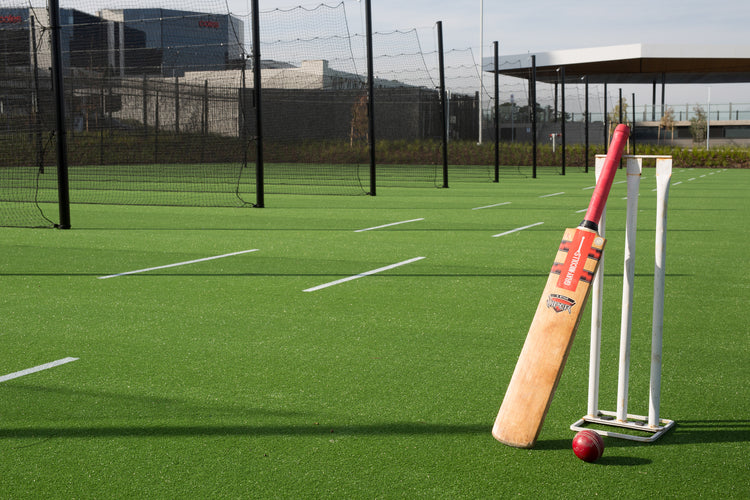Synthetic cricket field with bat, stumps, and ball on artificial turf sports surface