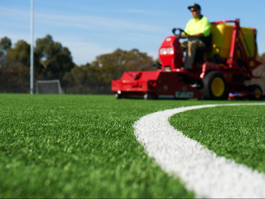 Artificial turf field maintenance with a ride-on machine on sports grass surface
