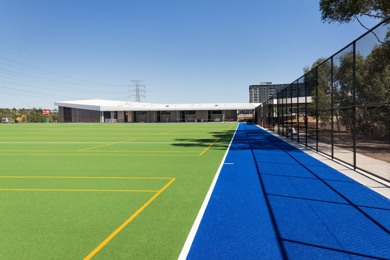Outdoor synthetic turf sports field with bright green surface and marked lines beside blue running track