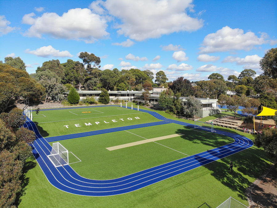 Synthetic turf sports field with blue running track at Templeton school under blue sky