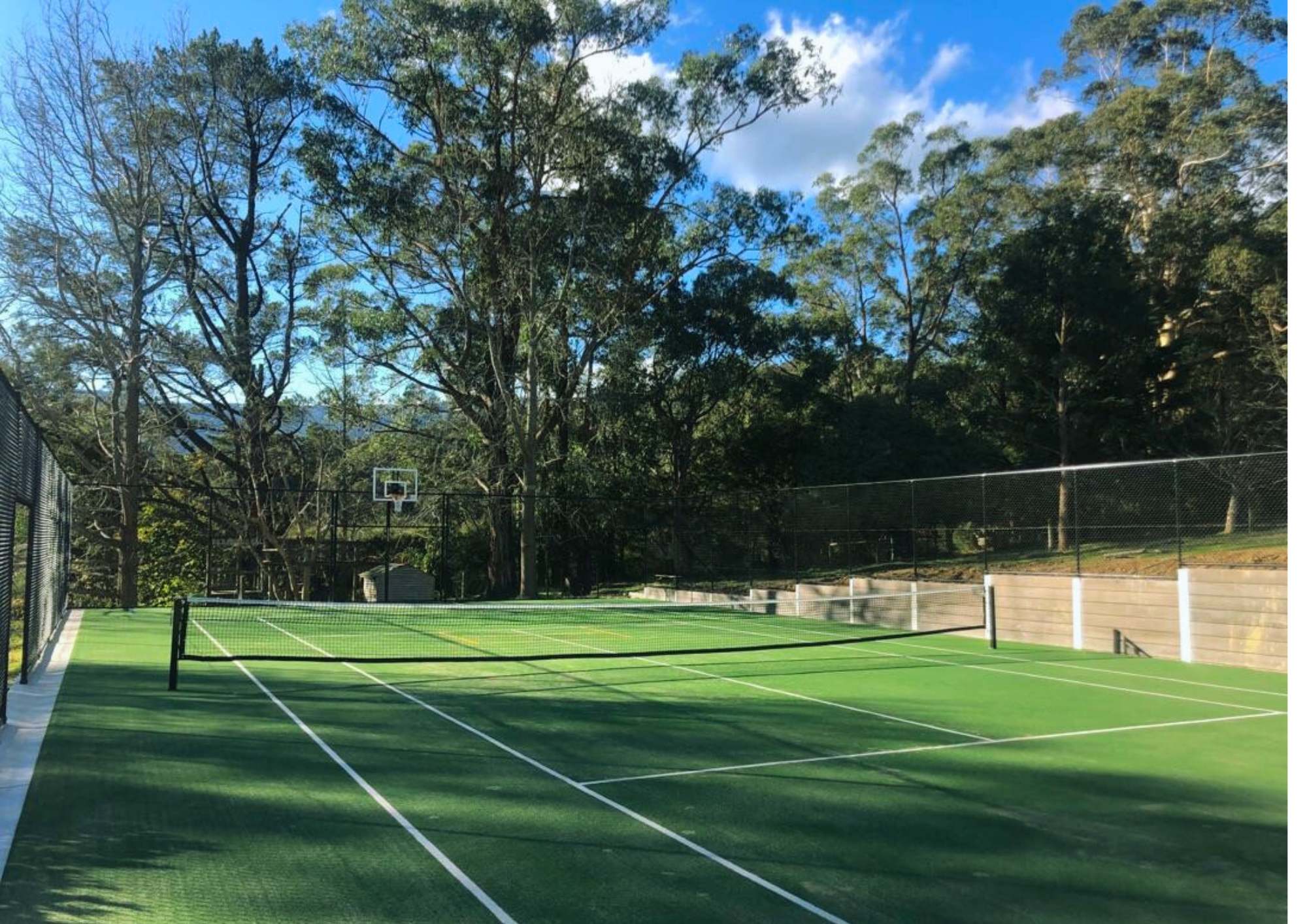 Synthetic tennis court installation in Melbourne surrounded by tall trees and fencing